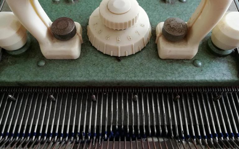 Extreme Close-up of a flatbed machine zooming into the carriage and needles with two lines of yarn on top of the needles.